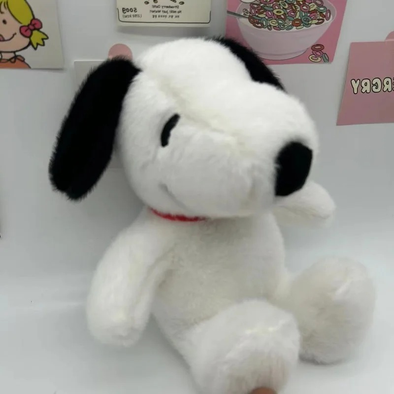 Snoopy de pelúcia sentado, de frente, com focinho preto e coleira vermelha