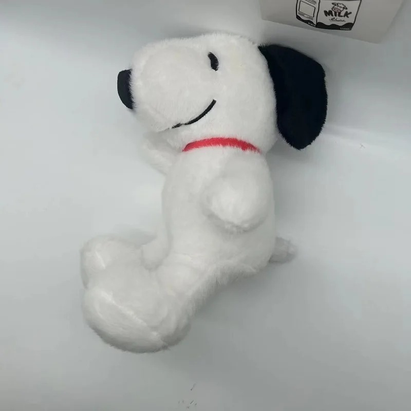 Snoopy de pelúcia de lado, com coleira vermelha, em fundo branco
