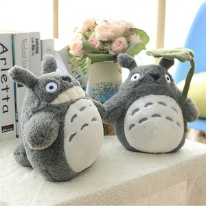 Duas pelúcias do Totoro cinza de barriga clara sobre uma mesa, uma delas com uma folha de lótus