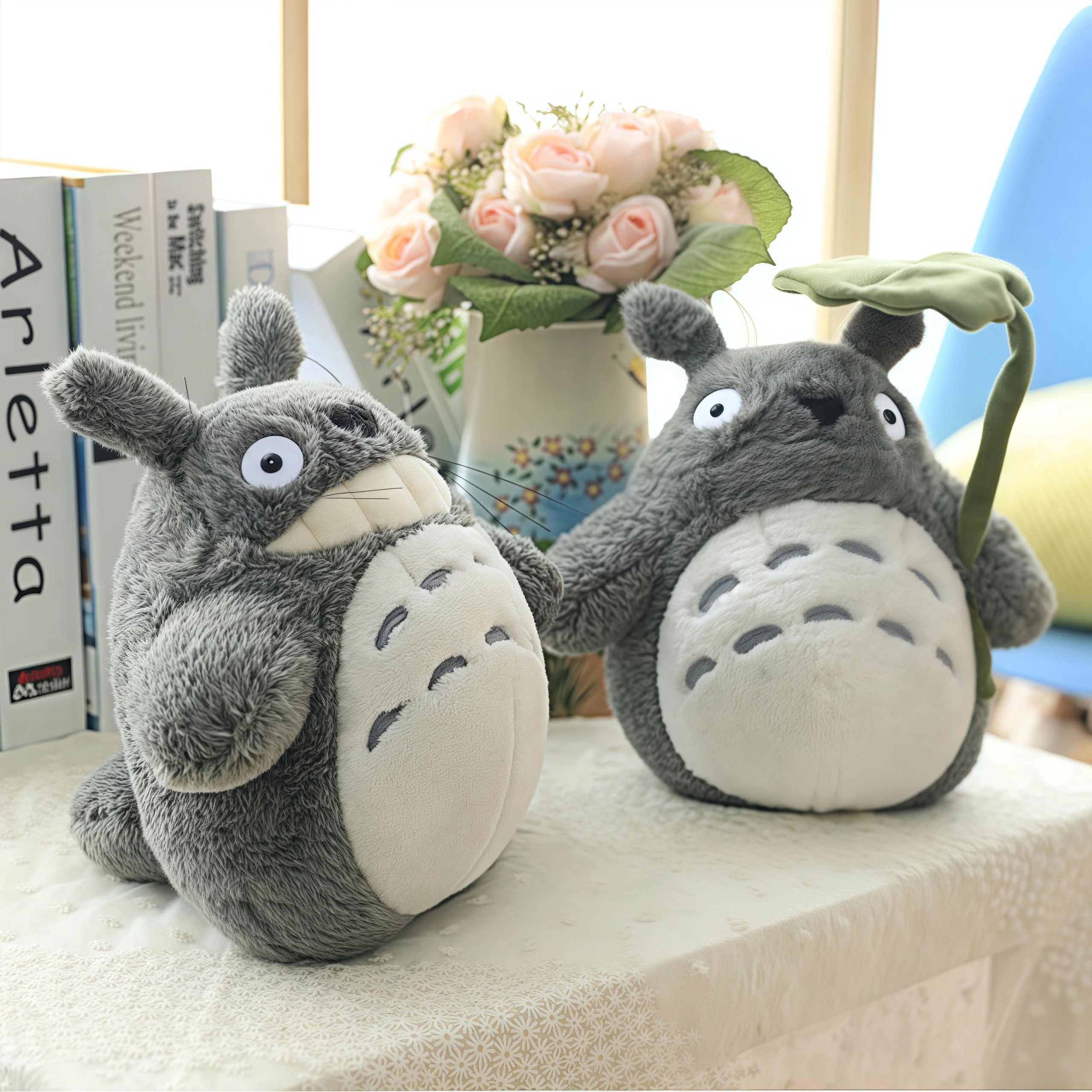 Duas pelúcias do Totoro cinza de barriga clara sobre uma mesa, uma delas com uma folha de lótus
