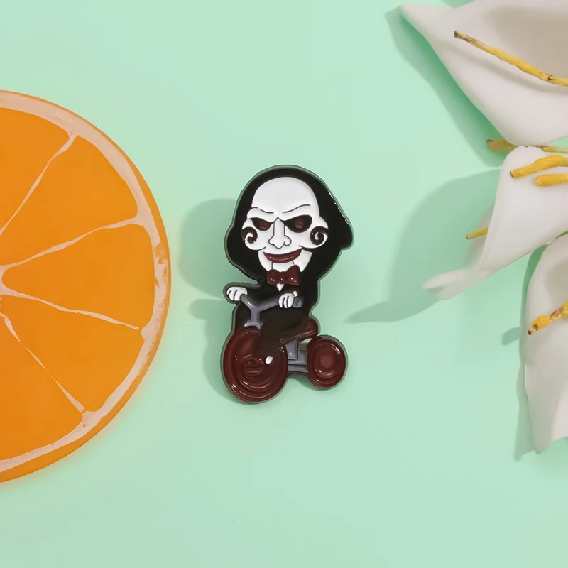 Pin do boneco Billy de Jogos Mortais ao lado de uma fatia de laranja e flores
