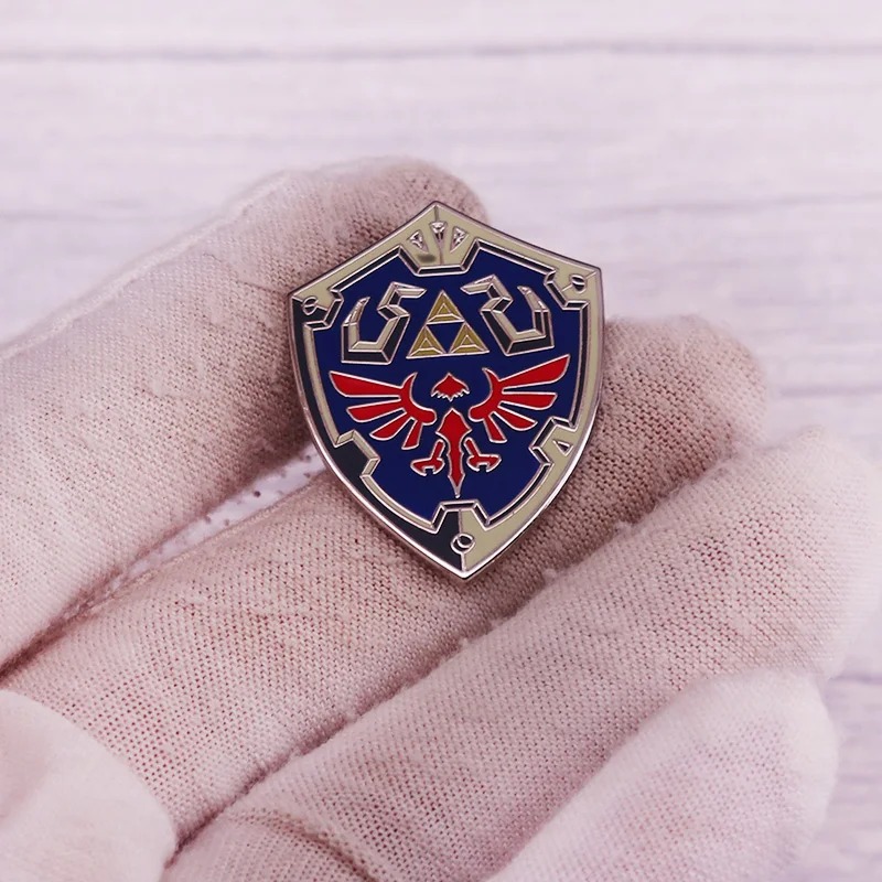 Broche do Escudo Hylian entre os dedos para mostrar o tamanho