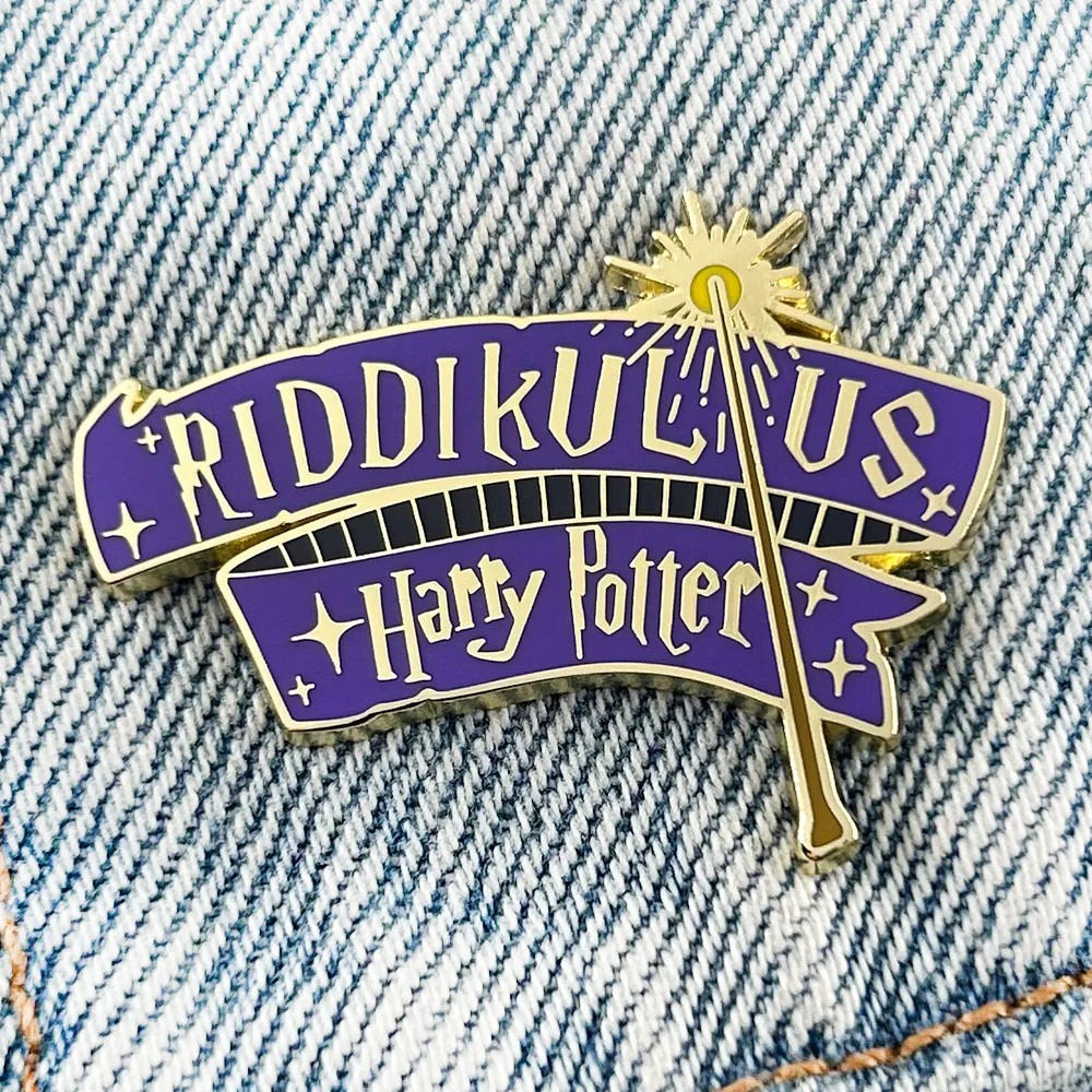 Pin esmaltado do feitiço Riddikulus, Harry Potter, em faixa roxa com varinha dourada, sobre jeans