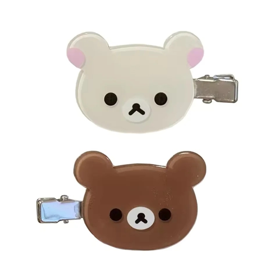 Presilhas do Rilakkuma, marrom, e da Korilakkuma, bege, com grampo de metal sobre fundo branco
