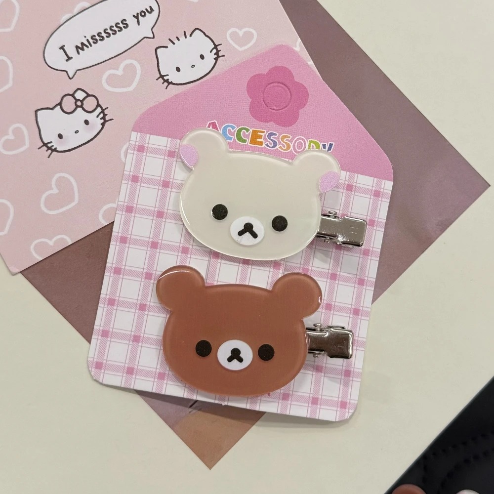 Presilhas de Rilakkuma e Korilakkuma presas a uma cartela rosa quadriculada