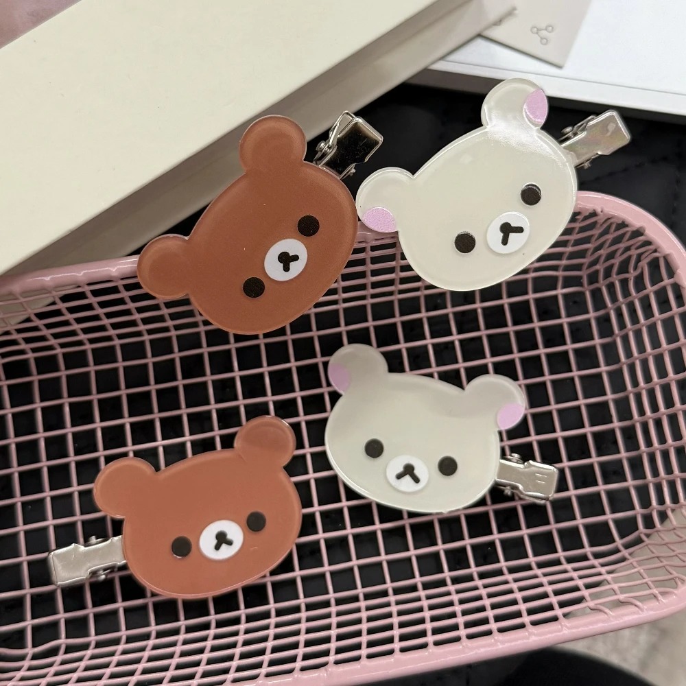 Quatro presilhas com cabeça de urso do Rilakkuma, em marrom e bege, sobre um cesto rosa