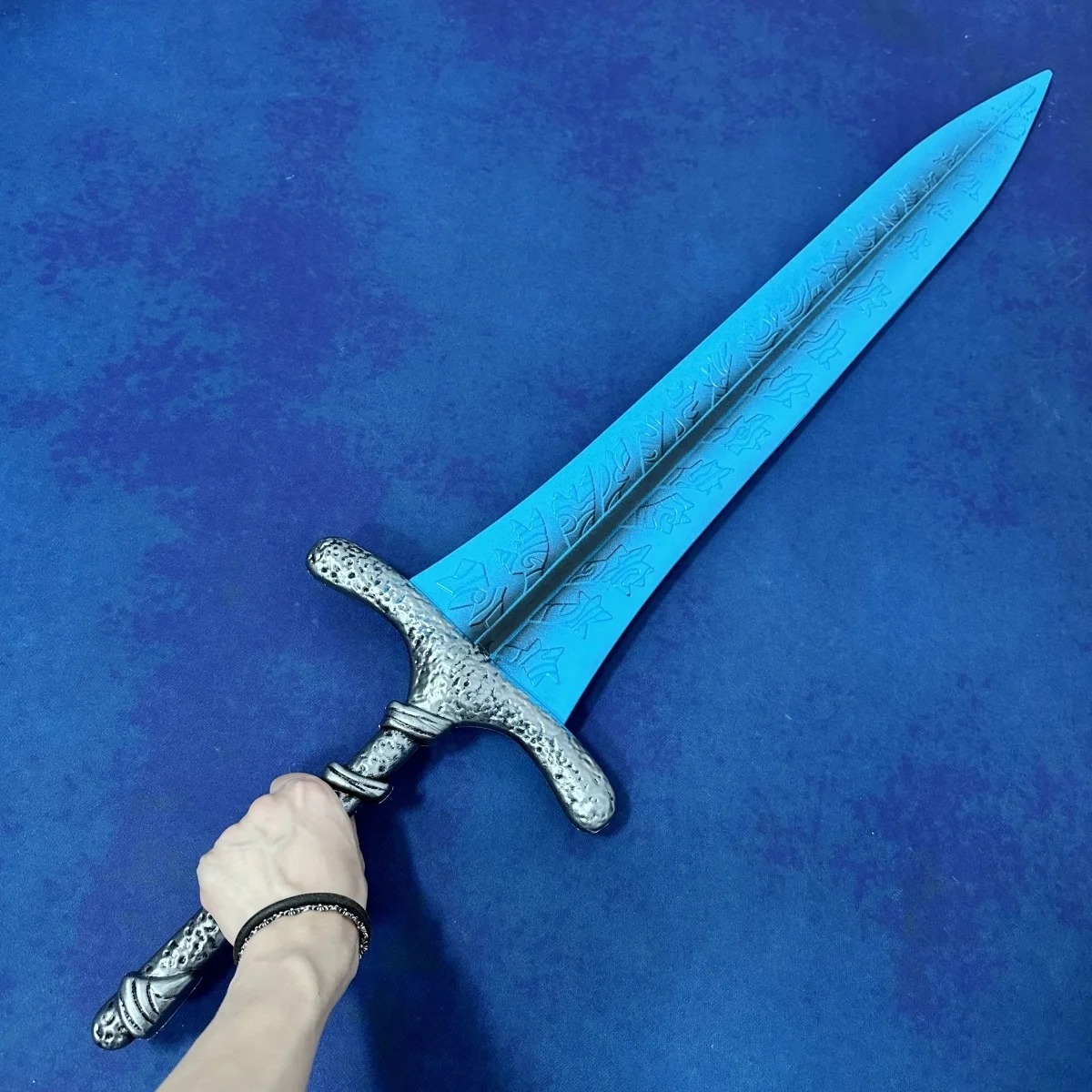 Mão segurando o cabo prateado da réplica da Dark Moon Greatsword para dar noção de escala