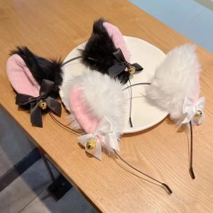 Três tiaras de orelhas de gato, pretas e brancas, com laço e guizo dourado, sobre uma mesa